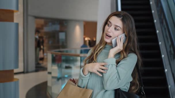 Молода красива біла дівчина жінка-покупка споживачів бізнес-леді, що стоїть в торговому центрі біля ескалатора, розмовляє по телефону, відповідаючи на дзвінок дружні розмови, тримаючи пакети з покупками — стокове відео
