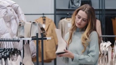 Beyaz çizmeli genç beyaz kadın tüketici kız müşterisi butik mağazasından siyah cuma zenginlik konsepti satışı hakkında şüphesi olan beyaz çizme seçiyor.