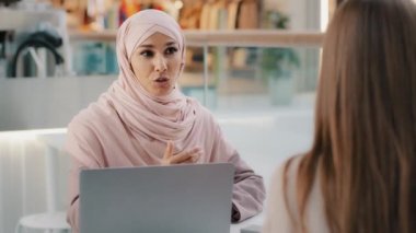 Genç Arap kadın danışman satış danışmanı büro masasında oturan banka çalışanı tanınmayan kız müşterilerine sözleşme imzalamayı öneriyor.