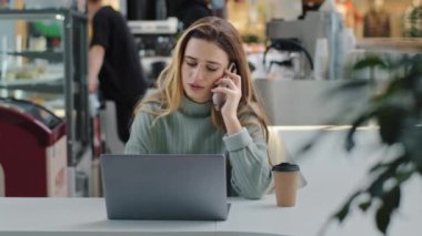 Ciddi iş kadını serbest yönetici öğrenci dizüstü bilgisayarla masada oturuyor. Telefonlara cevap veriyor. İş arkadaşlarıyla tartışıyor.