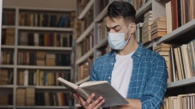 Koruyucu maskeli İspanyol erkek öğrenci, devlet üniversitesi kütüphanesinde kitap okuyarak sınav eğitimine hazırlanan yeni bilgilere odaklanıyor.