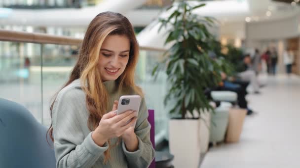 Νεαρή όμορφη ευτυχισμένη καυκάσια γυναίκα χιλιετή κορίτσι κάθεται στο δωμάτιο κοιτάζοντας την οθόνη του κινητού τηλεφώνου χρησιμοποιώντας το app chatting αγοράζει online ψώνια βλέποντας βίντεο λαμβάνουν μήνυμα στο smartphone γραπτών μηνυμάτων — Αρχείο Βίντεο
