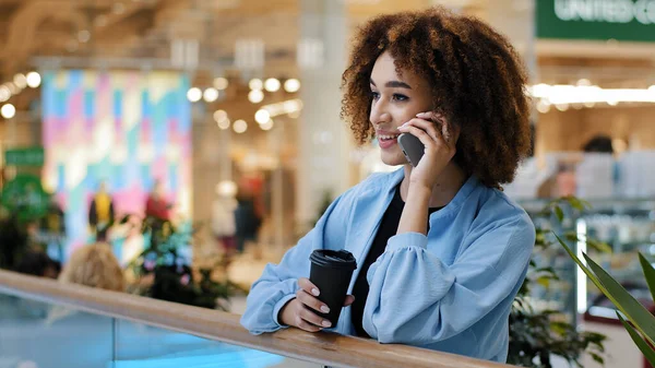 Framgångsrik afrikansk amerikansk affärskvinna talar mobiltelefon telefonsamtal tjänst online shopping bokning gör ordning med smartphone dricka te kaffe i köpcentret företag gratis wifi tech — Stockfoto