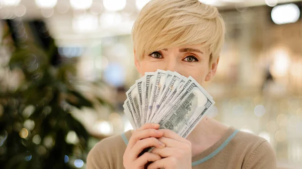 Glücklich wohlhabende erfolgreiche erwachsene Geschäftsfrau mittleren Alters blickt in die Kamera, die einen Fan von Geld hält, das sich hinter Dollarnoten versteckt, die den Gewinn aus einem Lohnsparkredit zeigen. — Stockfoto