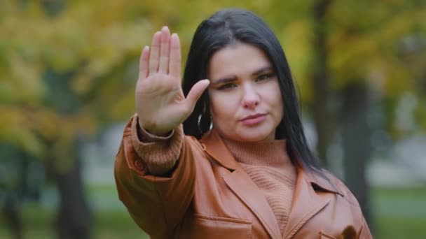 Muchacha hispana joven y seria de pie al aire libre sostiene la palma de la mano mostrando el gesto de dejar de mirar a la cámara protestando contra el abuso familiar violencia doméstica racismo discriminación luchando por los derechos de la mujer — Vídeos de Stock