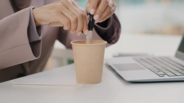 손을 거의 알아볼 수없는 여성 사업가가 책상에 앉아 랩탑을 들고 설탕을 일회용 컵에 붓고 있다. — 비디오