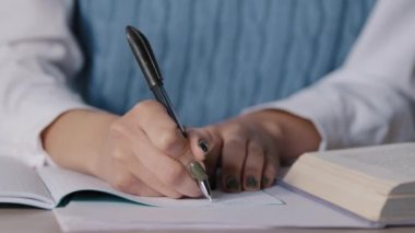 Yakın plan, kimliği belirsiz kadın öğrenci masasında oturuyor. Ödev defterine notlar yazıyor. Sınava hazırlanıyor.