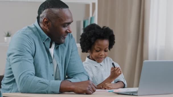 Prendersi cura del padre afro-americano aiutando la piccola figlia studentessa a fare i compiti a casa genitore adulto o tutor spiegando ai processi educativi del computer bambino su laptop e-learning apprendimento a distanza a casa — Video Stock