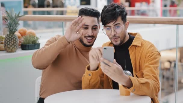 Zwei junge arabische Jungs, die mit Freunden auf den Bildschirm schauen und sich per Handy-App per Webcam unterhalten, bloggen lächelnd winkende Grüße und kommunizieren per Videokonferenz mit der Kamera auf dem Smartphone — Stockvideo