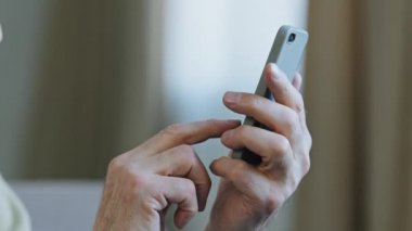 Yakın plan yaşlı adam elinde telefonla mesaj yazıyor. Uzaktan iletişim için online sipariş uygulaması yapıyor. Yetişkin büyükbaba modern teknolojiden hoşlanıyor.