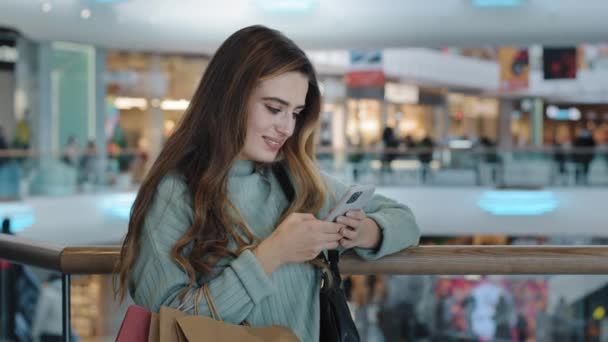 Frau Verbraucher weiblich Shopaholic Mädchen steht in Einkaufszentrum mit Paketen suchen in Handy E-Commerce Auswahl Produkt Geschenk Kleidung Online-Shop App Buchung bestellen Rabatt Verkauf kaufen — Stockvideo