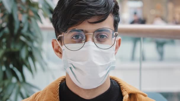 Retrato de close-up jovem em pé dentro de casa olhando para a câmera posando usando máscara médica descartável devido ao surto de pandemia de vírus covid19 consciente protegendo seu conceito de segurança e proteção da saúde — Vídeo de Stock