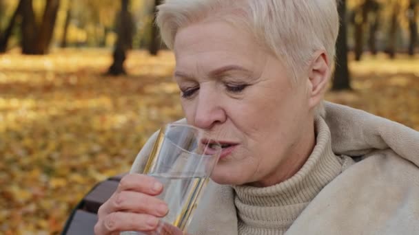 特写快乐老年妇女喝一杯新鲜清澈过滤的水保持平衡微笑积极成熟的奶奶在秋天公园休息解渴健康的老年生活方式理念 — 图库视频影像