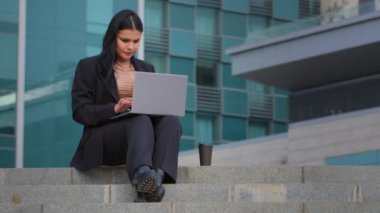 Genç İspanyol iş kadını dışarıda oturuyor, bilgisayarla fazla mesai yapıyor bilgisayar uygulaması kullanıyor, internette geziniyor, aşırı çalışmadan dolayı ekranı kapatıyor.