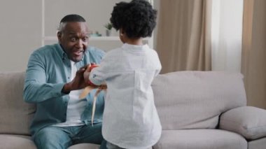Küçük afro amerikan kızı saklama kutusu sevgili babasına doğum gününde hediye veriyor ya da babalar gününü kutluyor. Mutlu baba kanepeye oturmuş küçük kıza sarılıyor güçlü aile kucaklıyor.