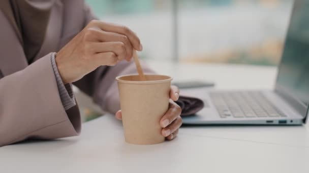 Close-up empresária irreconhecível sentado no trabalho na mesa de escritório com laptop mãos femininas misturando açúcar em copo de papel descartável bebendo café da manhã ou chá desfrutando de bebida quente durante o intervalo para almoço — Vídeo de Stock