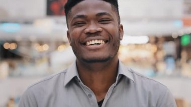 Yakın plan genç Afro-Amerikalı adam kameraya bakıyor gülümsüyor dişlek gülümseme duygusal olumlu adam iyi haberlere gülüyor ya da komik şaka samimi neşeli duygular neşe kahkahaları sergiliyor