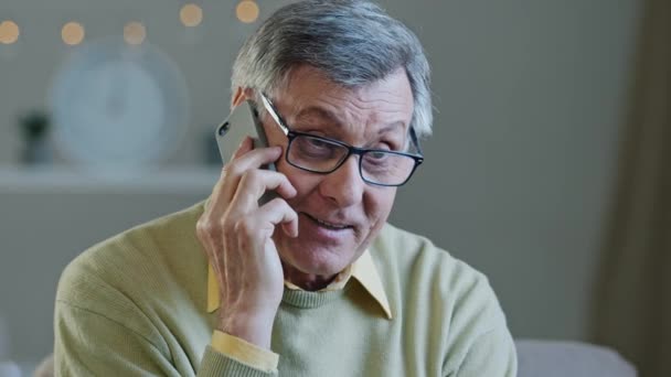 Portret siwy starszy mężczyzna w okularach rozmawiać przez telefon uśmiechnięty dziadek czatować wesoło korzystać mobilne dzielenie się dobrą wiadomością z dziećmi szczęśliwy wiek męski odpoczynek w domu cieszyć się przyjemną rozmowę — Wideo stockowe