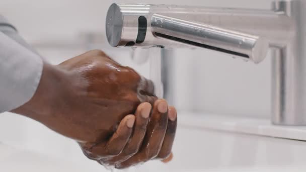 Close-up young unrecognizable african american man businessman washes hands in modern bathroom slow motion rinsing dirty hands under warm water over sink concept daily hygiene protection from viruses — Stock Video