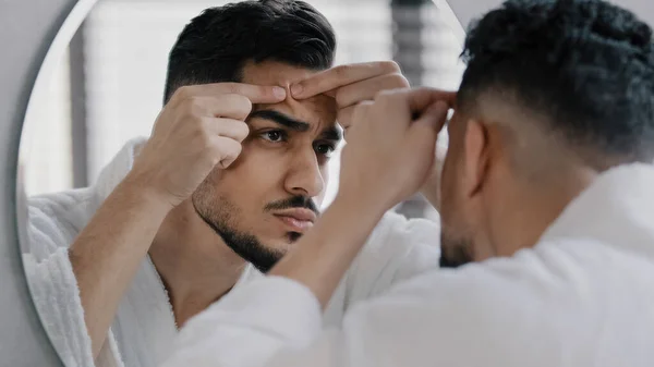 Mutsuz Arap Arap sakallı adam banyo aynasına bakıyor ve yüz sorunu olan sivilceler için endişeleniyor. Yüzüne sivilce değdiren endişeli milenyum adamı. Hayal kırıklığına uğramış siyah noktalar.