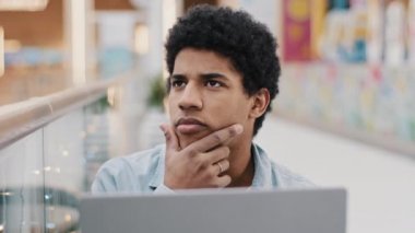 Düşünceli, Afro-Amerikan erkek, çenesini ovuşturan, çözüm düşünen, strateji geliştiren, dizüstü bilgisayarlı, erkek yazar, düşünce güçlüğü çeken yeni bir yazar.