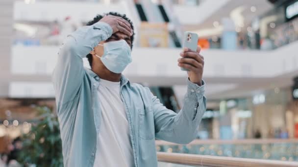Африканський американець, одягнений в медичну захисну маску в приміщенні карантинної коїдальної пандемії дивлячись на мобільний телефон, втратив свою відмову від повідомлення через погане розчарування в новинах. — стокове відео