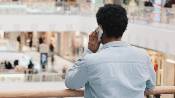 Πίσω όψη από πίσω αγνώριστη αφροαμερικανός επιχειρηματίας άντρας φοιτητής φίλος πελάτη στέκεται στο εμπορικό κέντρο χώρο της εταιρείας μιλάμε στο κινητό τηλέφωνο απομακρυσμένη διαπραγμάτευση διαβούλευση με το smartphone — Αρχείο Βίντεο