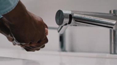 Yakın plan tanınmayan Afro-Amerikan evli adam umumi tuvalette lavabo otomatiği kullanıyor. Erkek eli, su sabunu koronavirüsü hijyen önleyici cilt bakımı konseptiyle yıkıyor.