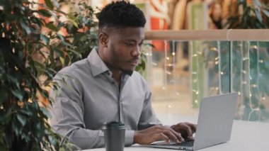 Odaklanmış genç Afro-Amerikan erkek serbest çalışan dizüstü bilgisayara dikkatle bakıyor iş e-posta yazıları yazıyor sosyal ağda bilgisayar uygulaması kullanarak sohbet ediyor.