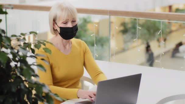 Feliz mujer de negocios de mediana edad en máscara médica sentado trabajando escribiendo correo electrónico en el ordenador portátil utilizando la nueva aplicación de ordenador que muestra pulgares hacia arriba gesto aprobación signo afirmación feliz con la tecnología moderna sonriendo — Vídeos de Stock