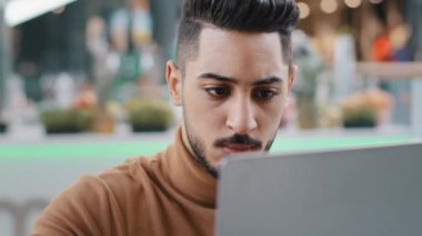 Yakın plan ciddi Arap erkek öğrenci serbest yazar dikkatle ekran dizüstü bilgisayarına bakar iş e-postası yazar sosyal ağlarda bilgisayar uygulaması kullanarak e-posta yazar.