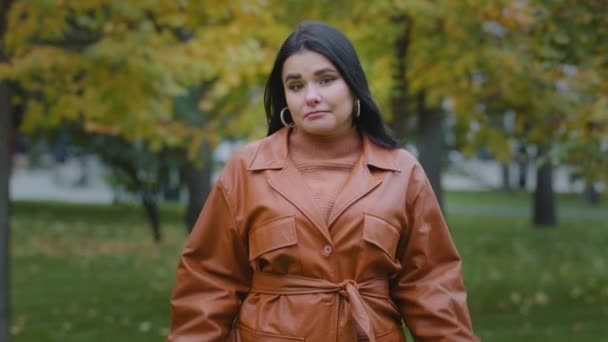 Jeune femme hispanique bouleversée perplexe debout à l'extérieur dans le parc haussant les épaules douteuse regardant la caméra incertaine ne sait pas quoi répondre fille incertaine faisant signe d'ignorance doute geste — Video