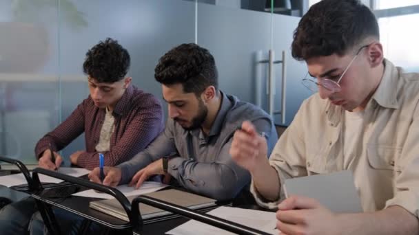 Frames grupo movimento diversos jovens estudantes sentam-se em fila na mesa em sala de aula concentrado escrever respostas de teste ou ensaio fazer anotações sobre papel tomando exame conceito de ensino superior na universidade ou escola — Vídeo de Stock