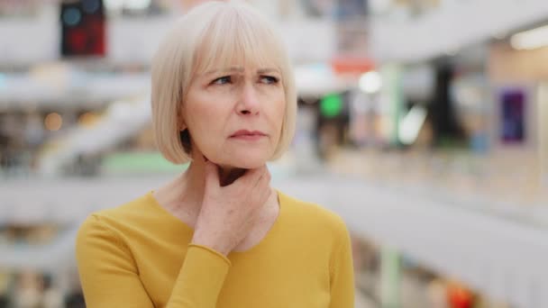 Madura de mediana edad mujer caucásica de pie en lugar público sosteniendo el cuello que sufre de dolor de garganta amigdalitis crónica sensación de pérdida no saludable voz asfixia espasmo quiere ayuda médica necesita tratamiento — Vídeo de stock