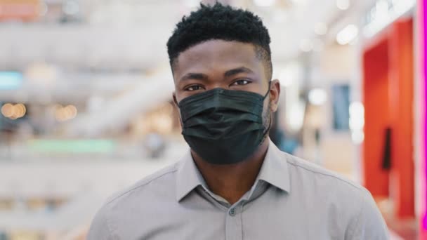 Närbild ung afrikansk amerikansk man i skyddande medicinsk mask promenader i köpcentret tittar på kamera förebyggande åtgärder covid19 virus under pandemi skyddas från bakterier epidemiska förebyggande koncept — Stockvideo