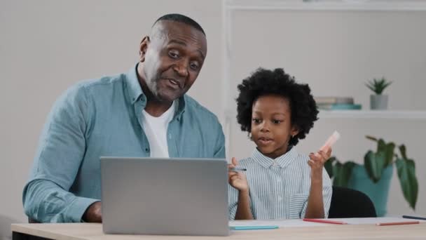 Feliz maduro afroamericano cariñoso padre sonríe ayudando a la niña colegiala con la tarea de estudio charlando en webcam con tutor utilizando el ordenador portátil saludando en línea e-learning durante la cuarentena — Vídeos de Stock