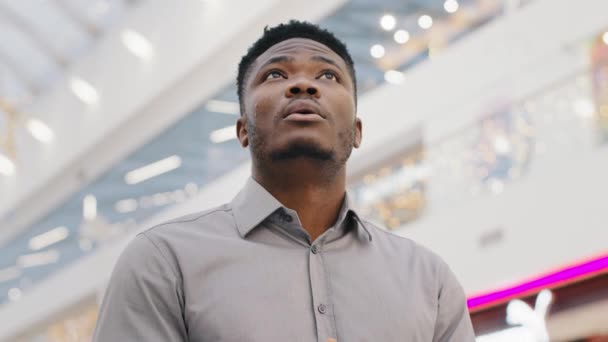 Close-up mannelijk portret jonge Afrikaan amerikaanse man student toerist staan in enorme winkels en entertainment center kijkt rond in verbazing verbijsterd door de schaal gebouw oprecht verrast bewondert — Stockvideo