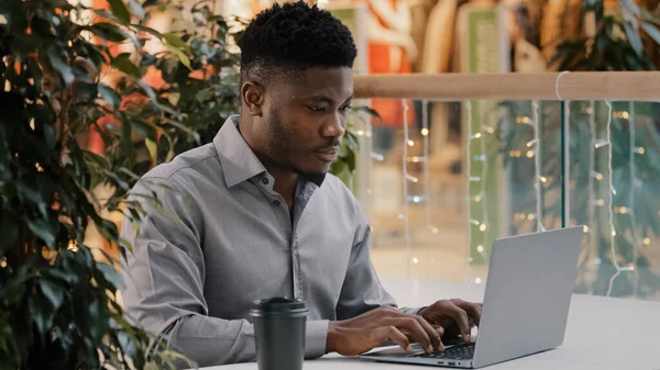 Focalisé jeune afro-américain mâle freelance regardant attentivement l'écran d'ordinateur portable travaillant à distance dactylographier email d'affaires écriture article bavarder sur le réseau social en ligne à l'aide d'une application informatique — Photo