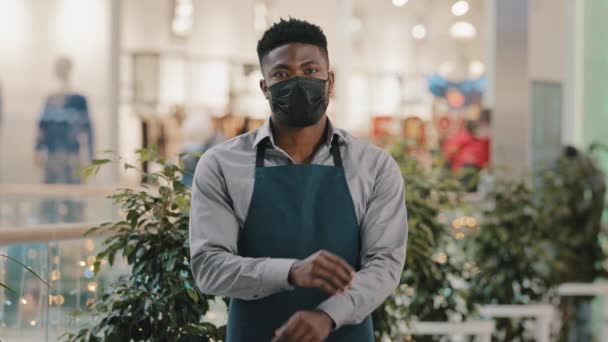 Fiducioso uomo afroamericano indossando maschera medica in piedi al chiuso guardando la fotocamera giovane cameriere in grembiule barista dipendente caffè bar proprietario venditore posa con le braccia incrociate concetto di piccola impresa — Video Stock