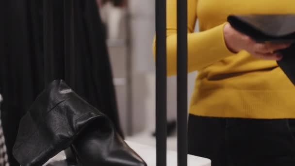 Közelkép kaukázusi elegáns középkorú nő ügyfél vásárló divatos butik ruhaüzlet kiválasztja cipőt tartja női fekete csizma gondosan néz minőségi termék vásárlás kedvezmény eladó — Stock videók