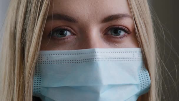 ผู้หญิงผิวขาวสวมหน้ากากทางการแพทย์ ตาสีน้ําเงิน กระพริบตา ผู้หญิงปกป้องจากไวรัสทางเดินหายใจ การกักกันไวรัสโคโรนาไวรัสโคโรนา — วีดีโอสต็อก