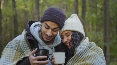 Yakın planda, mutlu turist çifti gezginler dışarıda çay içerler sıcak bir şeyler içerler ekose altında sarılırlar gülümseyerek keyifli bir iletişimin keyfini çıkarırlar romantik randevular doğada kucaklaşır.