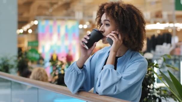 Bem-sucedida mulher de negócios afro-americana falando telefone celular atender serviço de chamada de compras on-line fazendo a ordem com smartphone beber chá café em empresa de shopping wifi gratuito — Vídeo de Stock