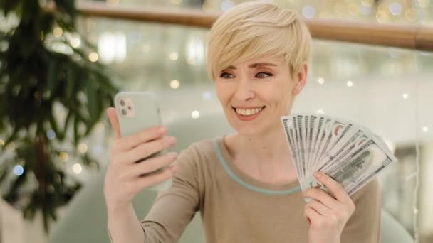 Reiche erfolgreiche Frau mittleren Alters, die Dollarscheine in der Hand hält und Videotelefonate aufzeichnet, spricht in die Handykamera — Stockvideo