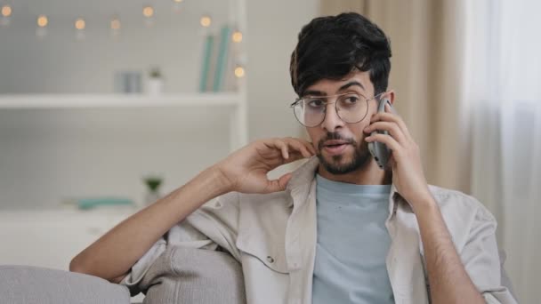 Hombre barbudo con gafas sentado en el sofá en casa hablando en la llamada de teléfono móvil charlando con amigos novia conversación remota comunicación conexión celular wifi gratuito tecnología 5g — Vídeo de stock