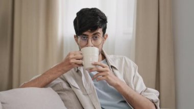 Arap sakallı milenyum adamı gözlüklü latin adam evde oturmuş lezzetli meyveli çayın tadını çıkarıyor kakao içiyor, kapuçino içiyor ve evet diyor. Kafa sallama konsepti.