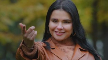 Yakın plan, baştan çıkarıcı, dost canlısı İspanyol bir kadın dışarıda kameraya bakıyor. Gülümsüyor, flört ediyor, parmaklarıyla cezbediyor.