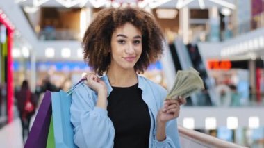 Mutlu Afro-Amerikan modacı kadın alışverişçi alışveriş delisi zengin bayan müşteri alışveriş torbaları alıyor ve yığınla parayla elbise indirimi indirimi teklif ediyor.