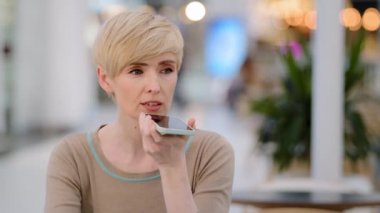 Orta yaşlı yetişkin bir kadın, Cafe Business 'taki hoparlörden ses tanıma mesajı kaydediyor. Sanal asistan uygulaması, akıllı telefon, telefon, mikrofon, cep telefonu, cep telefonu yardımı kullanıyor.