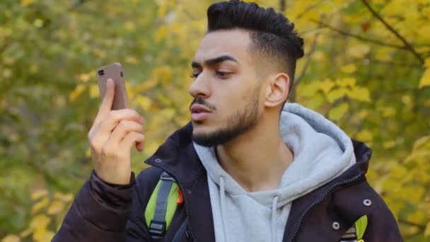 Joven parado al aire libre se quedó atrás del grupo turístico perdido en madera viajando con la mochila respondiendo a la llamada móvil sin conexión frustrada mirando a la pantalla del teléfono inteligente preocupado por el problema de Internet — Vídeo de stock